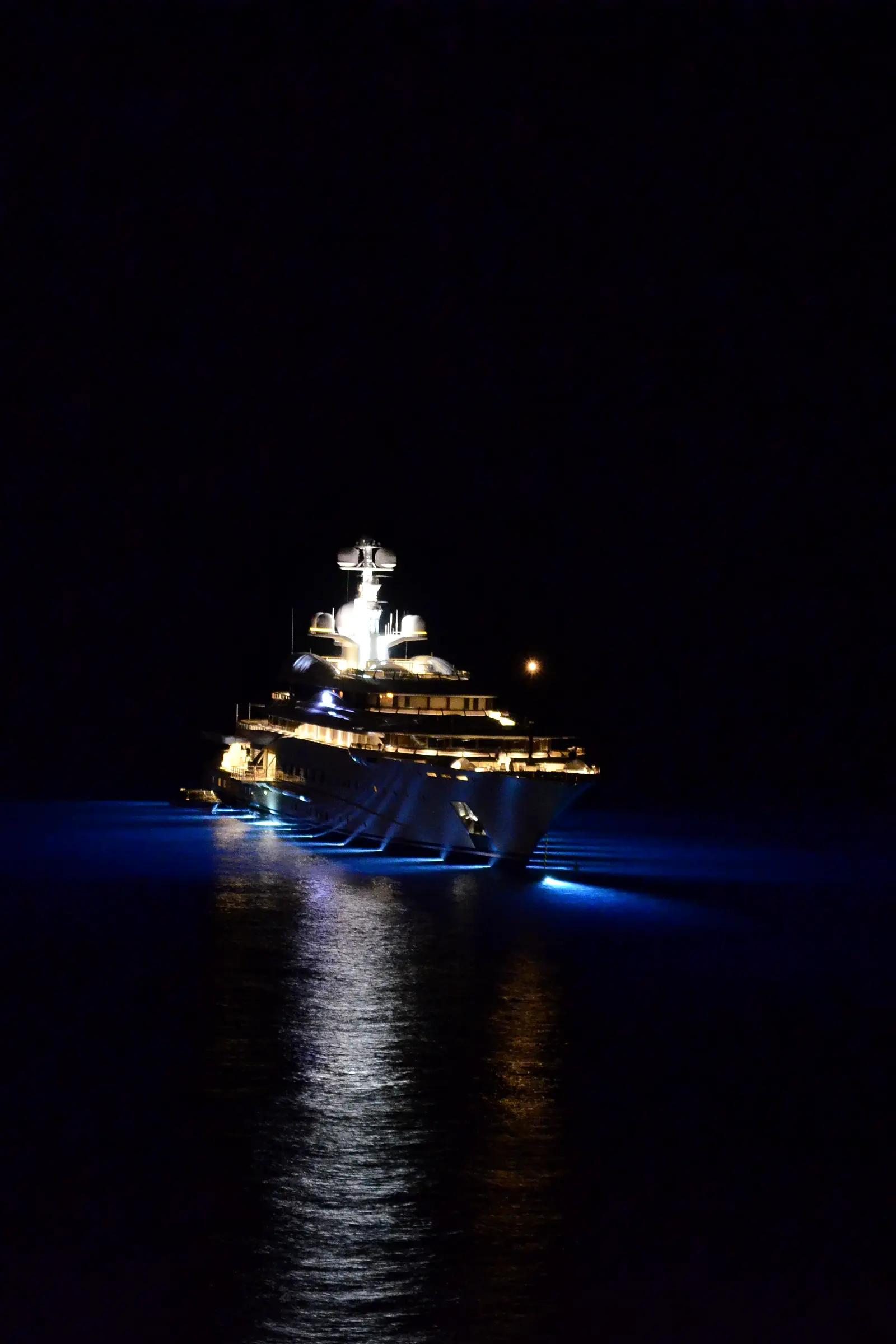 Superyacht lit up at night, reflected on the dark sea